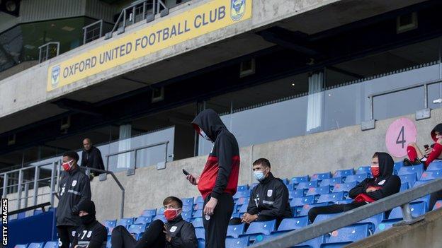 Crewe players wait in the stands before a postponed League One fixture at Oxford United