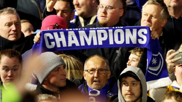 Portsmouth fan holds a scarf emblazoned with 'champions'