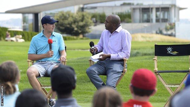 Jordan Spieth and Damon Hack sit in chairs on a golf course and talk into microphones