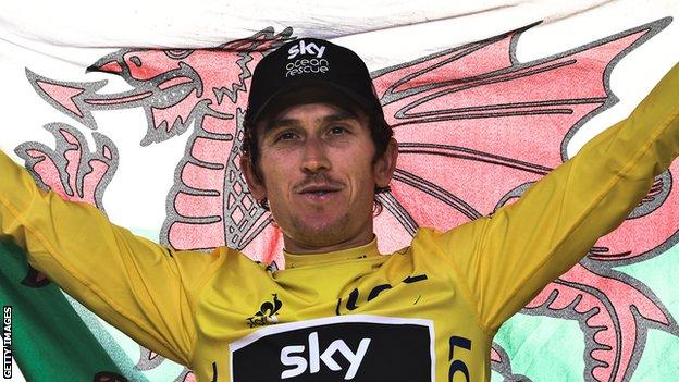 Geraint Thomas holds the Wales flag aloft while wearing the yellow jersey on the podium in Paris