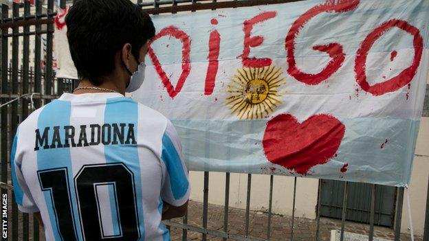 A fan wearing a Maradona Argentina shirt looks at a tribute in Buenos Aires