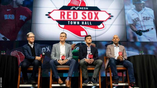 John Henry sits on a stool on stage at a Boston Red Sox fans' event alongside three other club officials