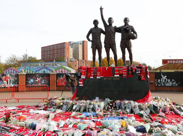 Scarves and flowers left in front of a statue of George Best, Denis Law and Bobby Charlton