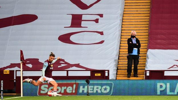 Jack Grealish takes a corner as a person in protective mask watches on