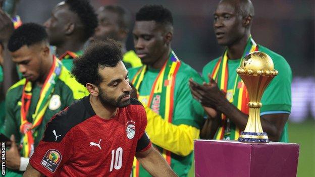 Mohamed Salah walks past the Nations Cup trophy