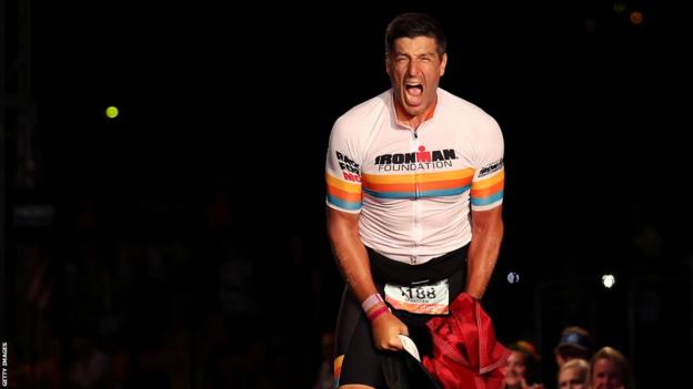 Sebastien Bellin celebrates clutching the Belgian flag after completing the 2022 Ironman in Kona