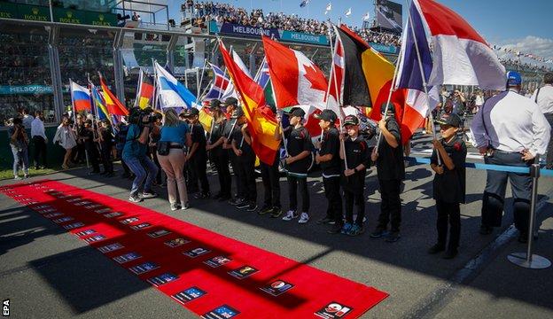 Children stand on the grid holding country flags
