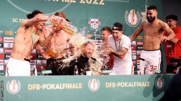 Domenico Tedesco, Head Coach of RB Leipzig is showered in beer by Yussuf Poulsen and teammates in the post match press conference after their sides victory during the final match of the DFB Cup 2022 between SC Freiburg and RB Leipzig