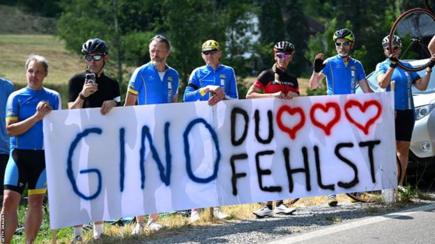 Fans hold a banner at the Tour de Suisse in tribute to Gino Mader, which reads 'you're missed'