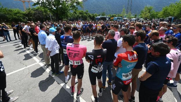 Riders and teams, stood in a large circle, are told of Gino Mader's death