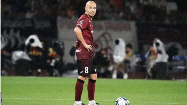 Andres Iniesta stands next to a football with his hands on his hips