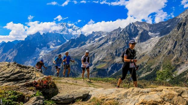 Competitors in UTMB against a backdrop of mountains and blue skies