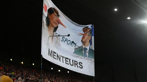 Liverpool fans' banner depicting Amelie Oudea-Castera and Gerald Darmanin as 