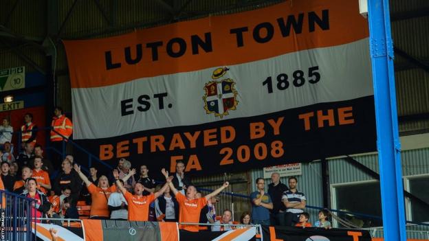 Luton Town fans with a banner that says 'Luton Town. Established 1885. Betrayed by the FA 2008.