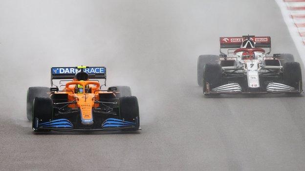 Lando Norris drives past an Alpha Romeo