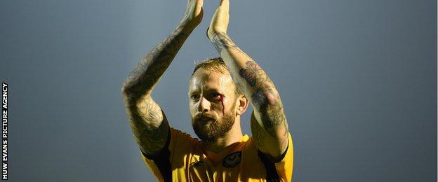 Sean Rigg shows off his tattoos on his arms while clapping Newport fans