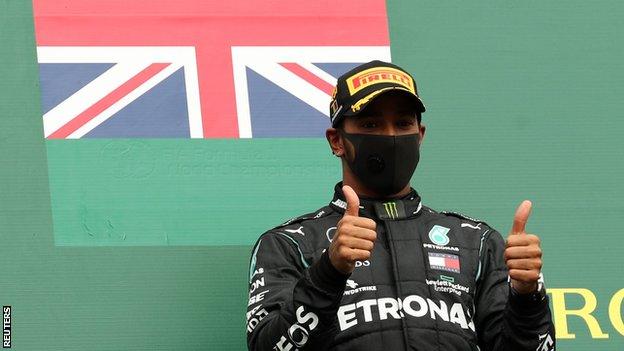 Lewis Hamilton holds two thumbs up on the podium