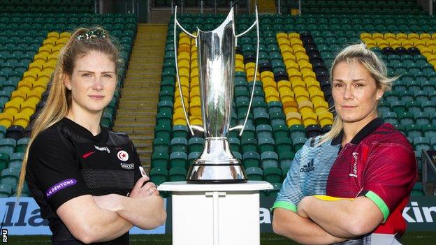 Lotte Clapp and Rachael Burford have their arms folded in front of the Premier 15s trophy