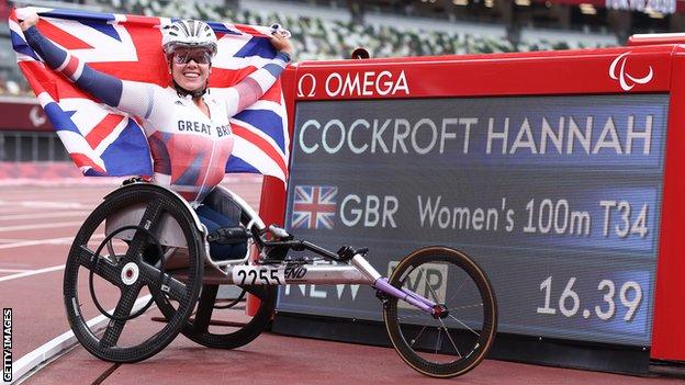 Hannah Cockroft holds up a British flag beside a screen showing her world record time