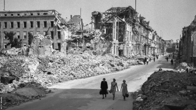 Three women walk along a Berlin street devastated by fighting in May 1945