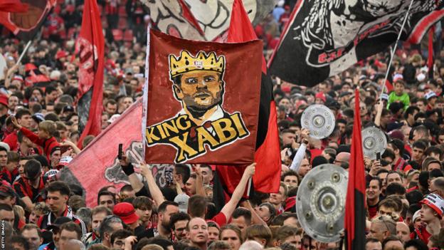 Leverkusen fans celebrate on the pitch with a banner of 'King Xabi' in tribute to boss Xabi Alonso
