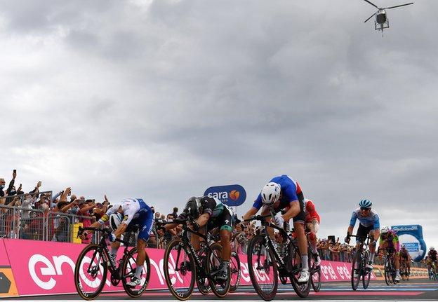 Riders finish stage four of the Giro d'Italia and the helicopter can be seen in the sky above