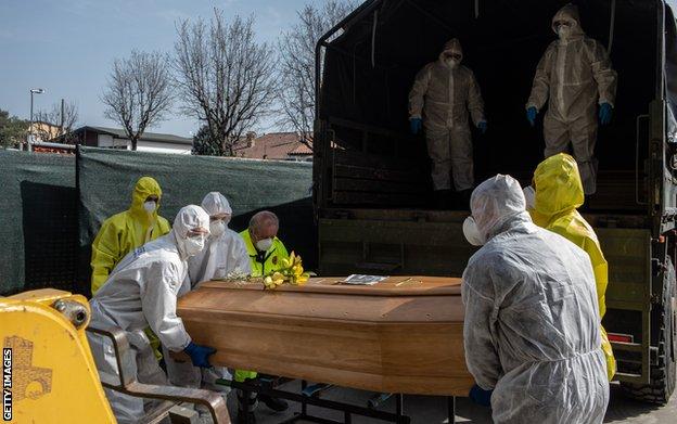 Carabinieri officers, wearing protective suits, lift a coffin on March 28, 2020 in Ponte San Pietro, near Bergamo