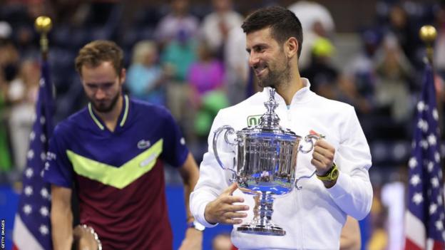 Novak Djokovic smiles as he lifts the US Open trophy