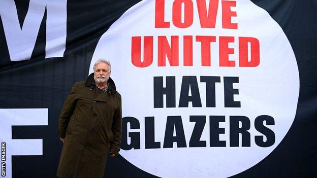Businessman Michael Knighton poses for a photo in front of a banner involving the Glazer ownership of Manchester United
