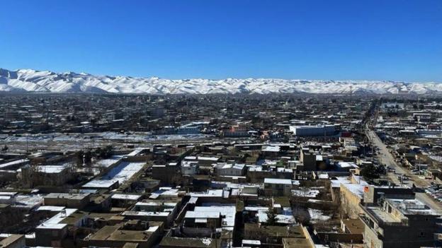Vue sur une petite ville afghane, des montagnes enneigées au loin et un ciel bleu
