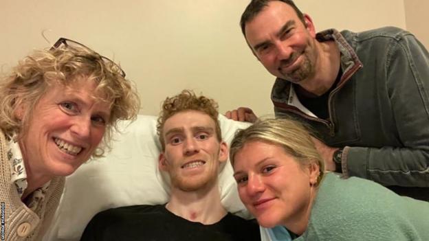 George Peasgood in a hospital bed alongside his parents and girlfriend