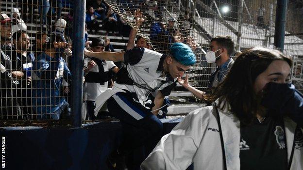 Gimnasia y Esgrima La Plata fans affected by tear gas jump the fence into the field