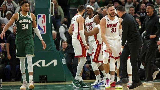 Max Strus celebrates with Miami Heat team-mates and staff while Giannis Antetokounmpo looks on
