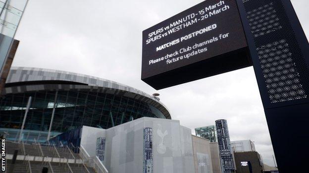 An exterior shot of the Tottenham Hotspur Stadium, with a sign in the foreground showing that the club's next two matches are postponed