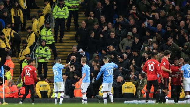 Manchester City's players intervene with City fans jeering and throwing objects at Manchester United players