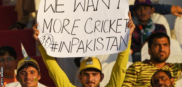 A fan holds a banner saying "We want more cricket in Pakistan"