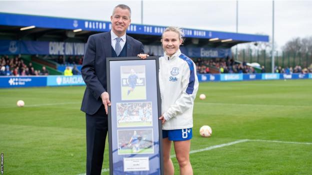 Izzy Christiansen recibe un marco de fotos de recuerdos después de hacer su aparición número 150 en la WSL