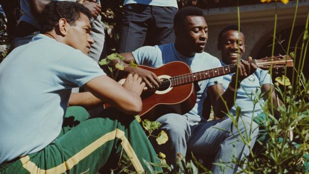 (Colour photograph) Pele plays an acoustic guitar surrounded by Brazil teammates before the team leaves for England to play in the 1966 World Cup.