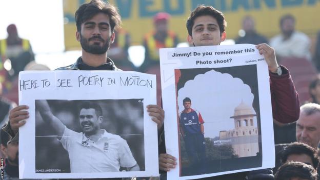 Two Pakistan fans hold us signs for England bowler James Anderson. One reads "Here to see poetry in motion" above a photo of Anderson. The other reads "Jimmy! Do you remember this photo shoot?" above a photo of Anderson in Lahore in 2005.