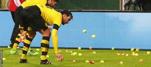 Dortmund players attempt to clear the pitch of tennis balls