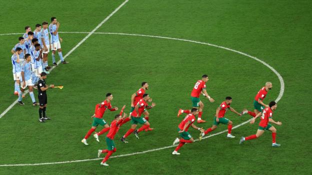 Morocco players run towards the penalty area from the centre circle to celebrate while the Spain players stand looking dejected in the background