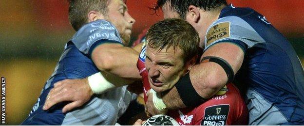 Hadleigh Parkes of Scarlets is tackled by Jack Carty and Denis Buckley