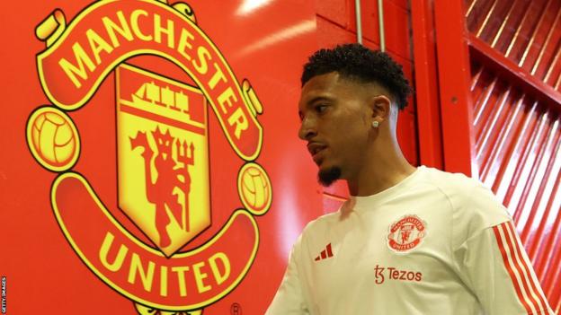 Manchester United winger Jadon Sancho next to the club's crest at Old Trafford