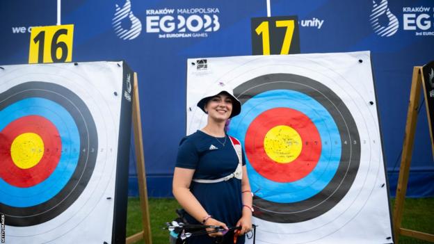 Penny Healey smiles and stands in front of archery target