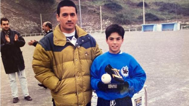 Mikel Arteta poses with a individual trophy and a family member as a boy