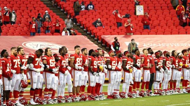 Kansas City Chiefs players link arms in a 'moment of unity' as the reduced crowd allowed into Arrowhead Stadium watch on