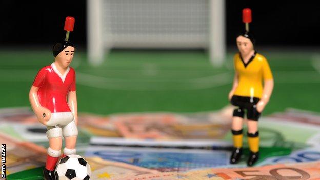 Figurines of footballers standing on a pile of cash