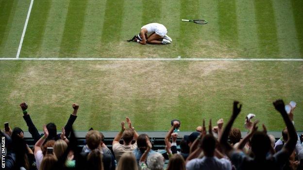 Emma Raducanu collapses to the ground holding her head in disbelief as the Wimbledon crowd jump up cheering