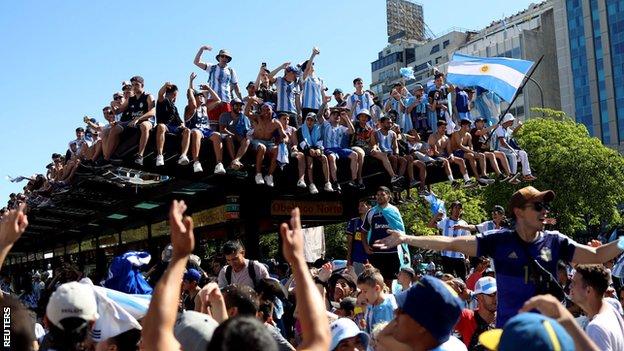 Argentina fans climb on top of a bus top in Buenos Aires' Plaza de la República as they waited for the team's arrival
