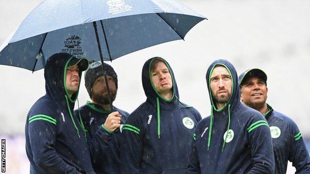 Members of the Irish team watch the rain fall from under an umbrella during the ICC Men's T20 World Cup match between Afghanistan and Ireland at Melbourne Cricket Ground
